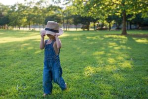 A boy in overalls and a hat walking across a lawn